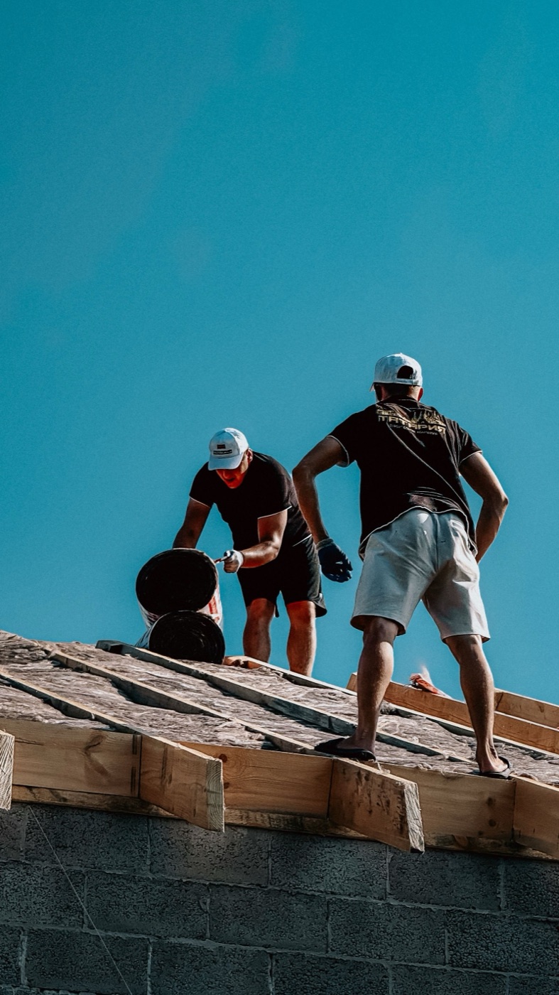 Two roofers working on a roof under a clear sky
